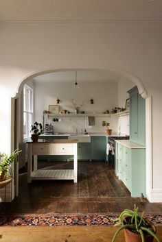 an archway leads into a kitchen with wooden floors and white walls, along with potted plants on the counter