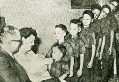 an old black and white photo of a group of children in front of a man