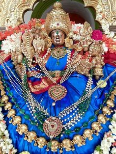 an idol is displayed in front of a building with flowers and decorations on the wall