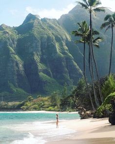 a woman standing on top of a sandy beach near the ocean with mountains in the background