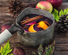 an old metal pot filled with liquid next to autumn leaves and apples on a wooden table