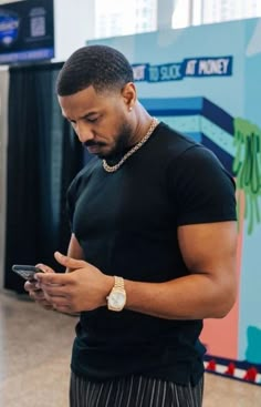 a man standing in an airport looking at his cell phone while wearing a watch on his wrist