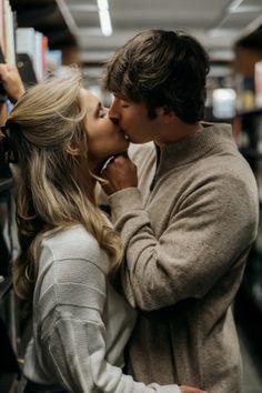 a man and woman kissing each other in front of bookshelves at a library