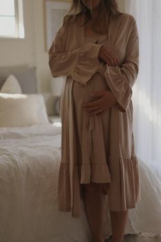 a pregnant woman standing on a bed with her hands in her stomach and looking at the camera