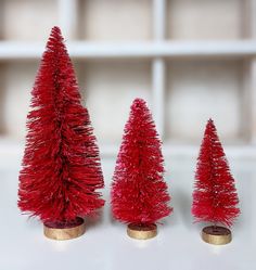 three small pink christmas trees sitting on top of a white table next to each other