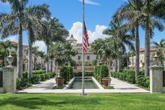 an american flag is flying in front of a building with palm trees and water fountain