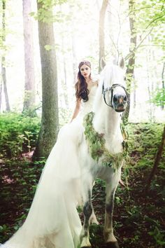 a woman in a wedding dress is riding a white horse through the woods with greenery