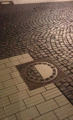 a manhole cover sitting on top of a brick road next to a street sign