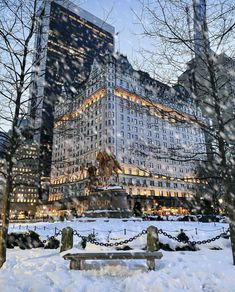 a snow covered park bench in front of a large building