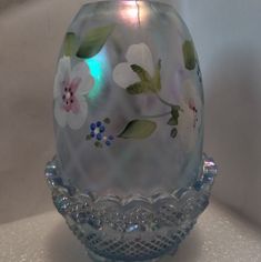 an egg with flowers painted on it sitting on a white table top next to a glass candle holder