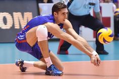 a volley ball player crouches down to catch the ball while people watch from the sidelines