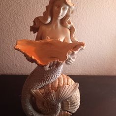 a statue of a mermaid holding a shell on top of a table