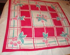 a red and white table cloth with cherries on it, sitting on top of a bed