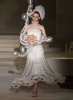 a woman is walking down the runway in a dress made out of balloons and pearls