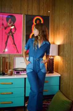 a woman standing next to a dresser in a room with pictures on the wall behind her