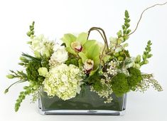 an arrangement of white flowers and greenery in a square glass vase on a white background