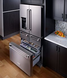 a stainless steel refrigerator and drawers in a kitchen with black cabinets, wood flooring and white marble countertops