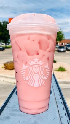 a pink starbucks drink sitting on top of a metal table next to a parking lot