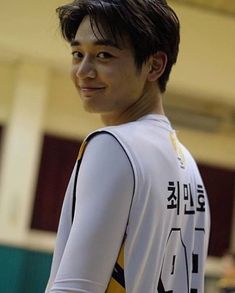 a young man holding a tennis racquet on top of a basketball court with other people in the background