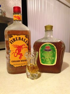 two bottles of alcohol sitting on top of a counter next to a glass filled with liquid