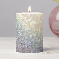 a white candle sitting on top of a table next to a pink vase and pencils