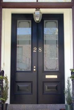 the front door is black and has two glass doors with numbers on them, along with potted plants