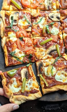 several square pizzas with different toppings on top of each one being held up by someone's hand