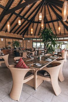 the inside of a restaurant with wicker tables and chairs, potted plants on either side