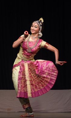 a woman in a pink and yellow dress dancing on stage with her hands out to the side