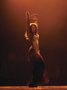 a belly dancer is performing on stage with her arms in the air and headdress