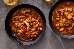 two black bowls filled with soup next to each other on top of a gray table