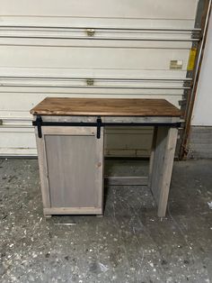 an old wooden desk sitting in front of a garage door with no one around it