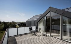 a wooden deck with chairs and tables on it next to a building that has glass walls