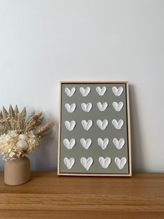 a wooden shelf with a vase and white flowers on it next to a gray wall