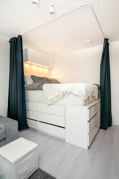 a white bed sitting under a window next to a gray couch and ottoman in a room