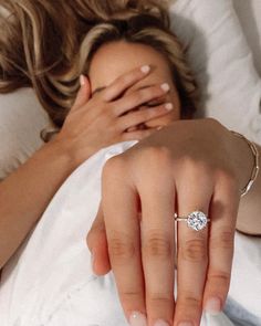 a woman is laying in bed with her hand on the pillow and wearing a diamond ring