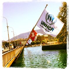 a flag flying over the water next to a bridge with a building in the background