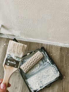 a person is holding a paint brush and painting on the floor in front of a wall