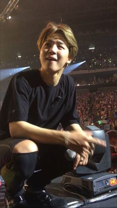 a young man sitting on top of a stool in front of a crowd at a concert