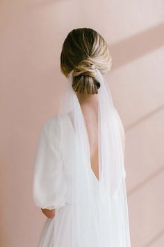 the back of a bride's dress with a veil on her head, standing against a pink wall