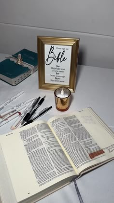 an open book sitting on top of a table next to a candle and some pens