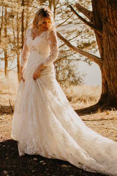 a woman in a wedding dress standing next to a tree and looking at the camera