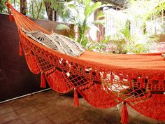 an orange hammock with tassels hanging from it's sides in a tropical setting