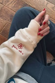 a woman with red nails is sitting on the floor and holding her hand up to her wrist