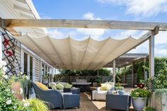 an outdoor covered patio area with furniture and potted plants on the deck, under a pergolated awning