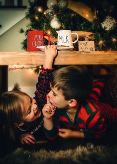 two young children laying on the floor next to a christmas tree and coffee mugs