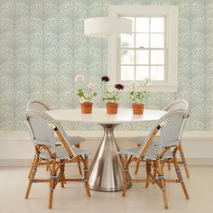 a white table with four chairs around it in front of a wallpapered room