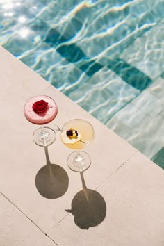 two wine glasses sitting next to each other near a swimming pool