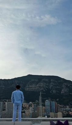 a man standing on top of a roof next to a tall building with a mountain in the background