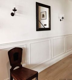 a wooden chair sitting in front of a mirror next to a wall with white waives